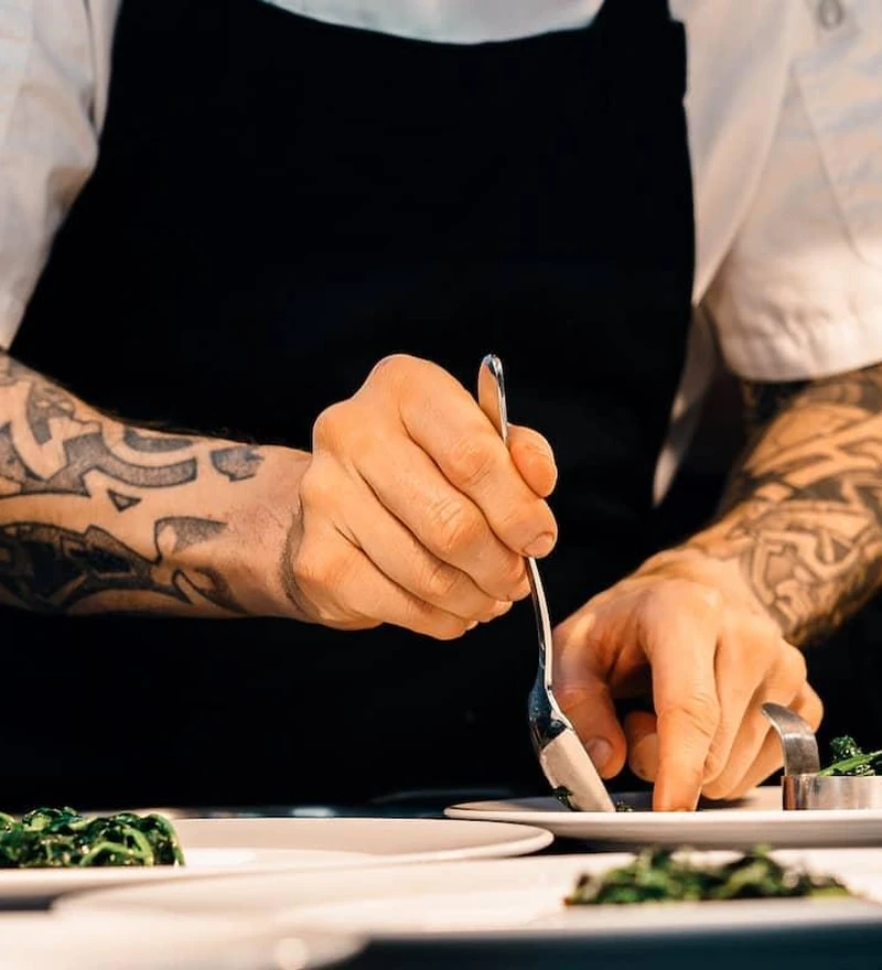 Mãos de um cozinheiro finalizando cuidadosamente um prato na cozinha